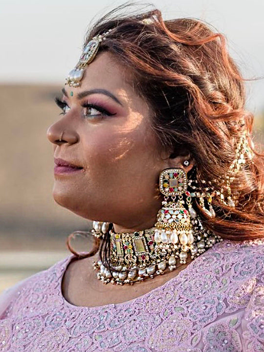 Women with intricate gold-toned jewelry including a detailed necklace, maang tikka, and earrings.